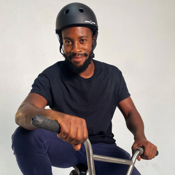 Omari Cato sitting on a BMX bike wearing a helmet, representing urban cycling and flatland BMX.